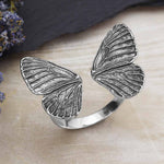 Silver butterfly wing ring on a wooden surface with dried flowers.