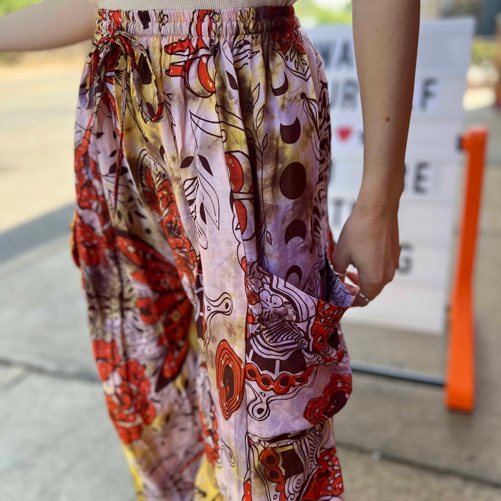 Model wearing red and purple tie-dye cargo pants with moon phase design close up view of pockets front view