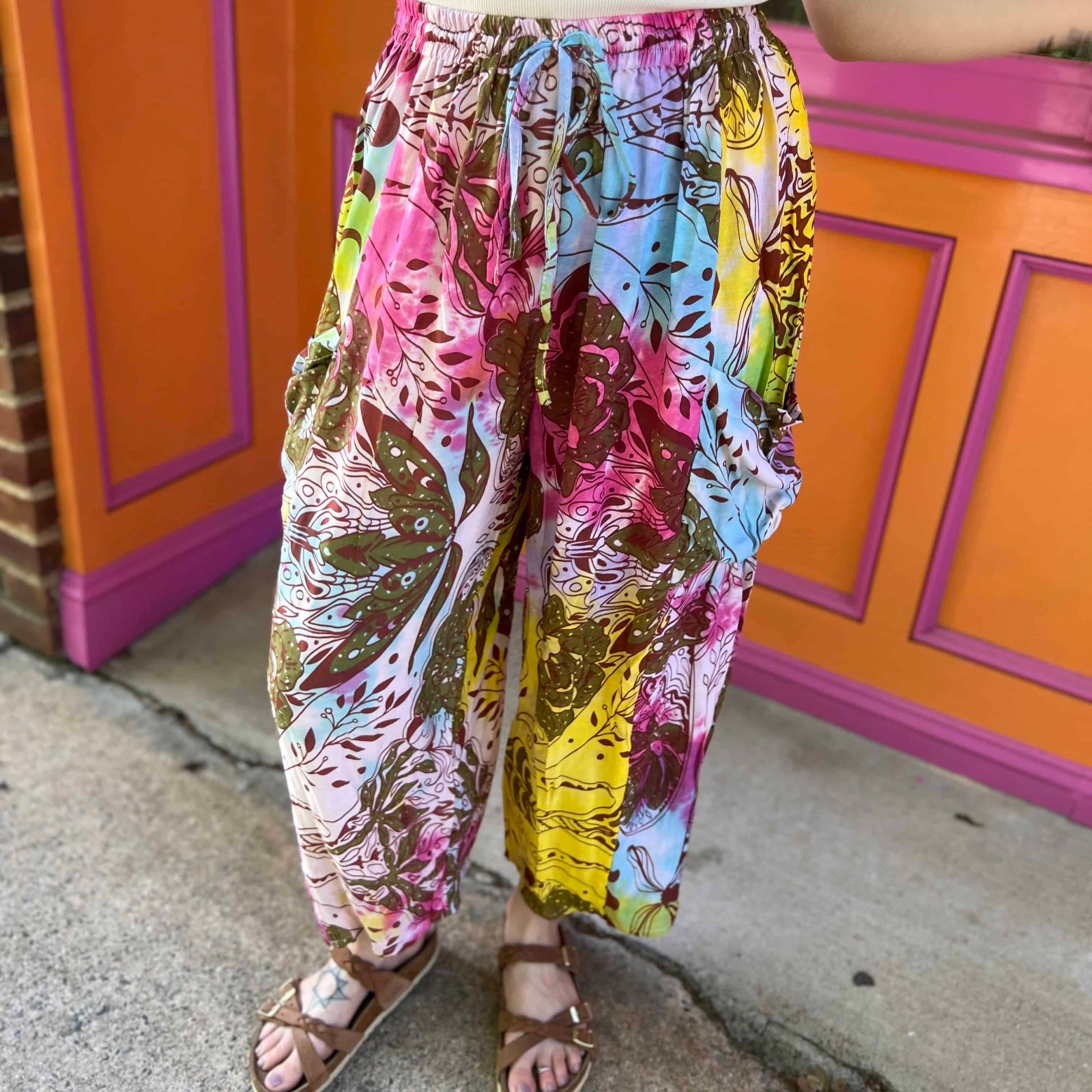 Rainbow tie-dye cargo pants with green floral moth pattern close up view showcasing pockets and shoes