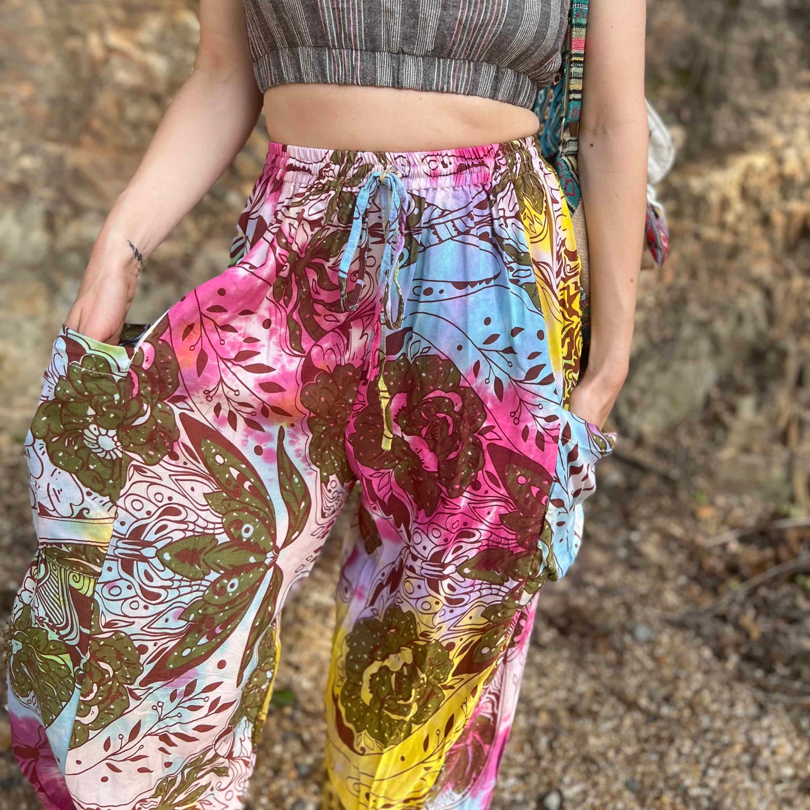 Rainbow tie-dye cargo pants with green floral moth pattern close up view with expanded hands in pockets