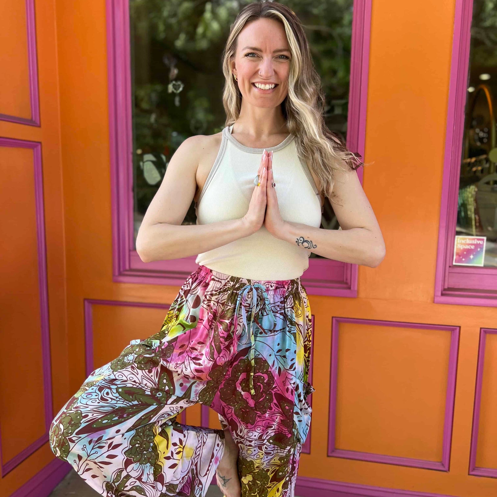 Rainbow tie-dye cargo pants with green floral moth pattern with model in yoga pose