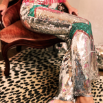 A woman wearing the Sequin Flare Thunderbolt Disco Pants with a pink fringe sequin top while sitting down in a velvet chair.