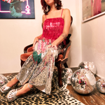 A woman wearing the Sequin Flare Thunderbolt Disco Pants with a pink fringe sequin top while sitting down in a velvet chair.