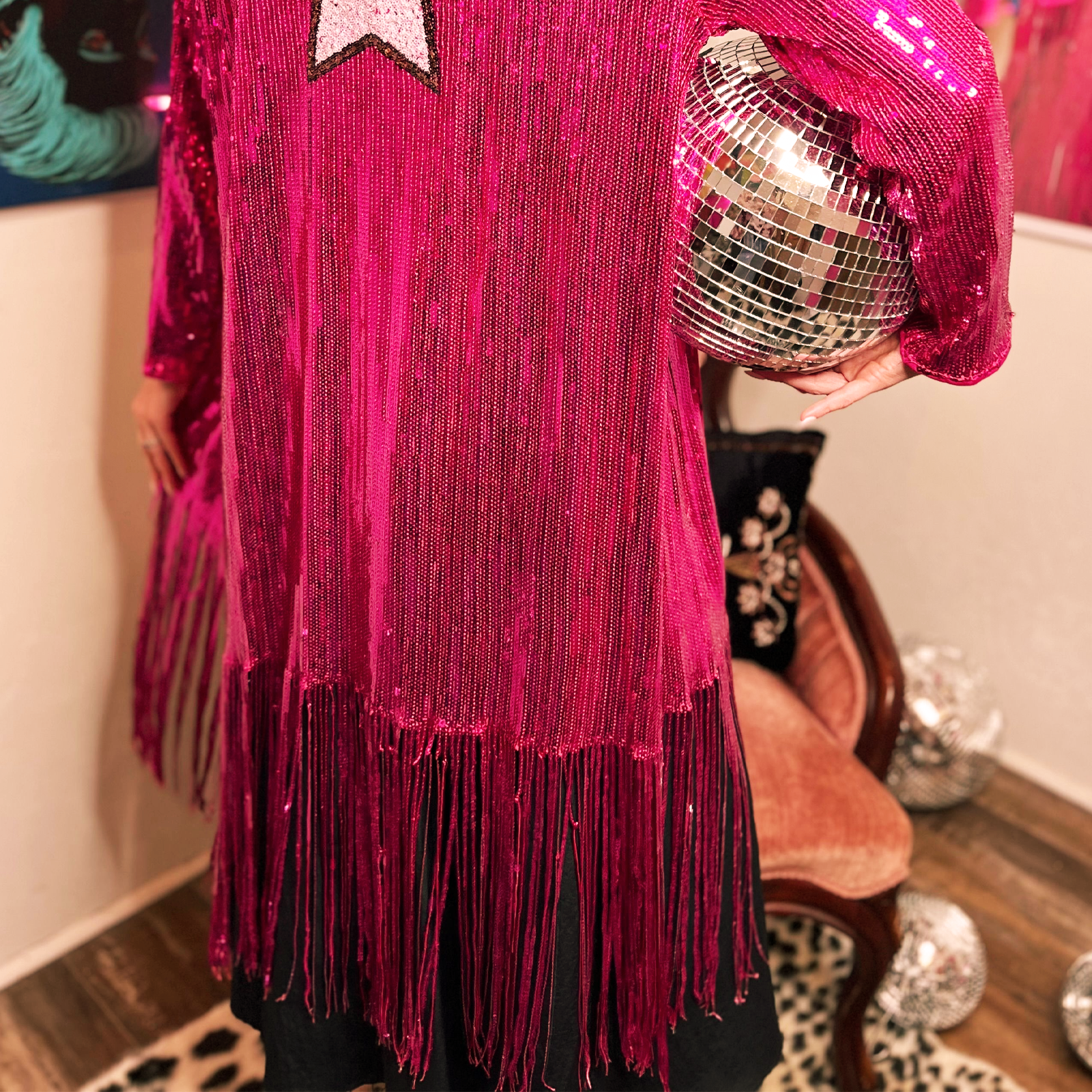 A woman wearing the Sequin Fringe Star Back Open Cardigan while holding a disco ball, and showing off the back.