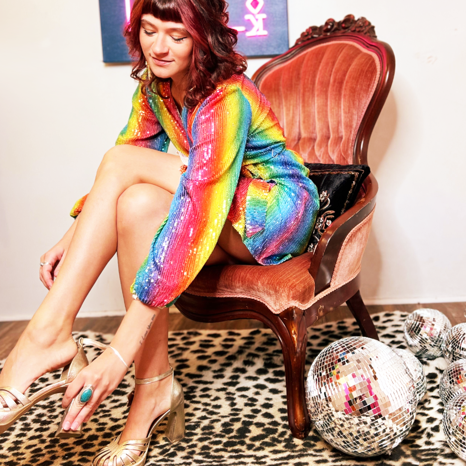 A woman sitting down and wearing the Disco Rainbow Wrap Dress.