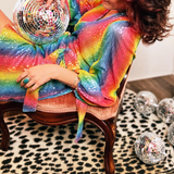 A woman sitting in a chair holding a disco ball and wearing the Disco Rainbow Wrap Dress.