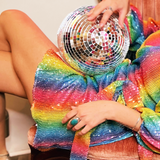 A woman sitting in a chair holding a disco ball and wearing the Disco Rainbow Wrap Dress.