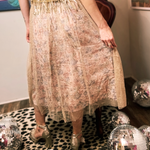 Someone wearing the Metallic Tulle Floral Maxi Skirt in front of a velvet chair and leopard print rug, showing off the back.