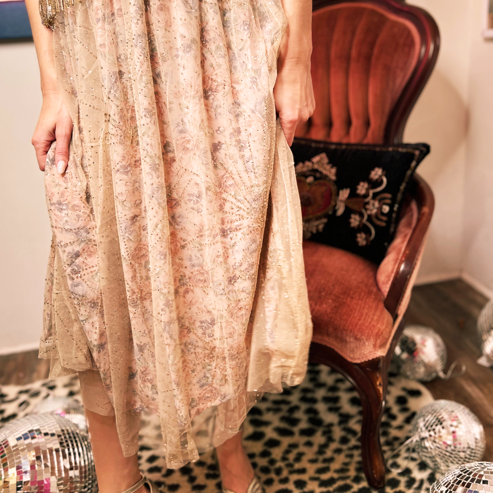 Someone wearing the Metallic Tulle Floral Maxi Skirt in front of a velvet chair and leopard print rug.