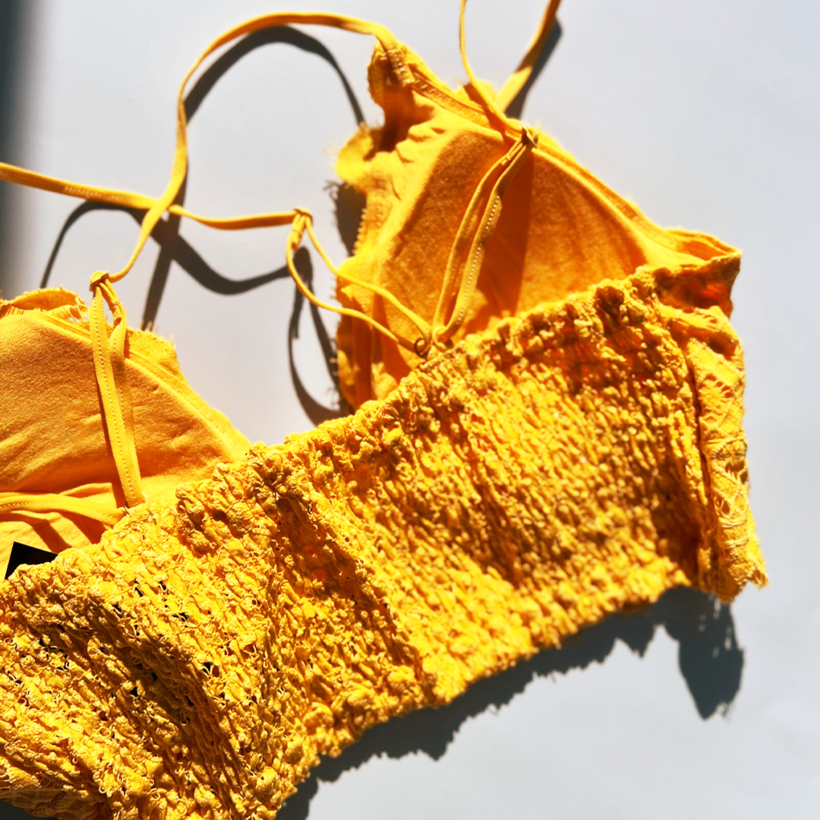 The mustard Criss-Cross Back Lace Bralette on a blue background.