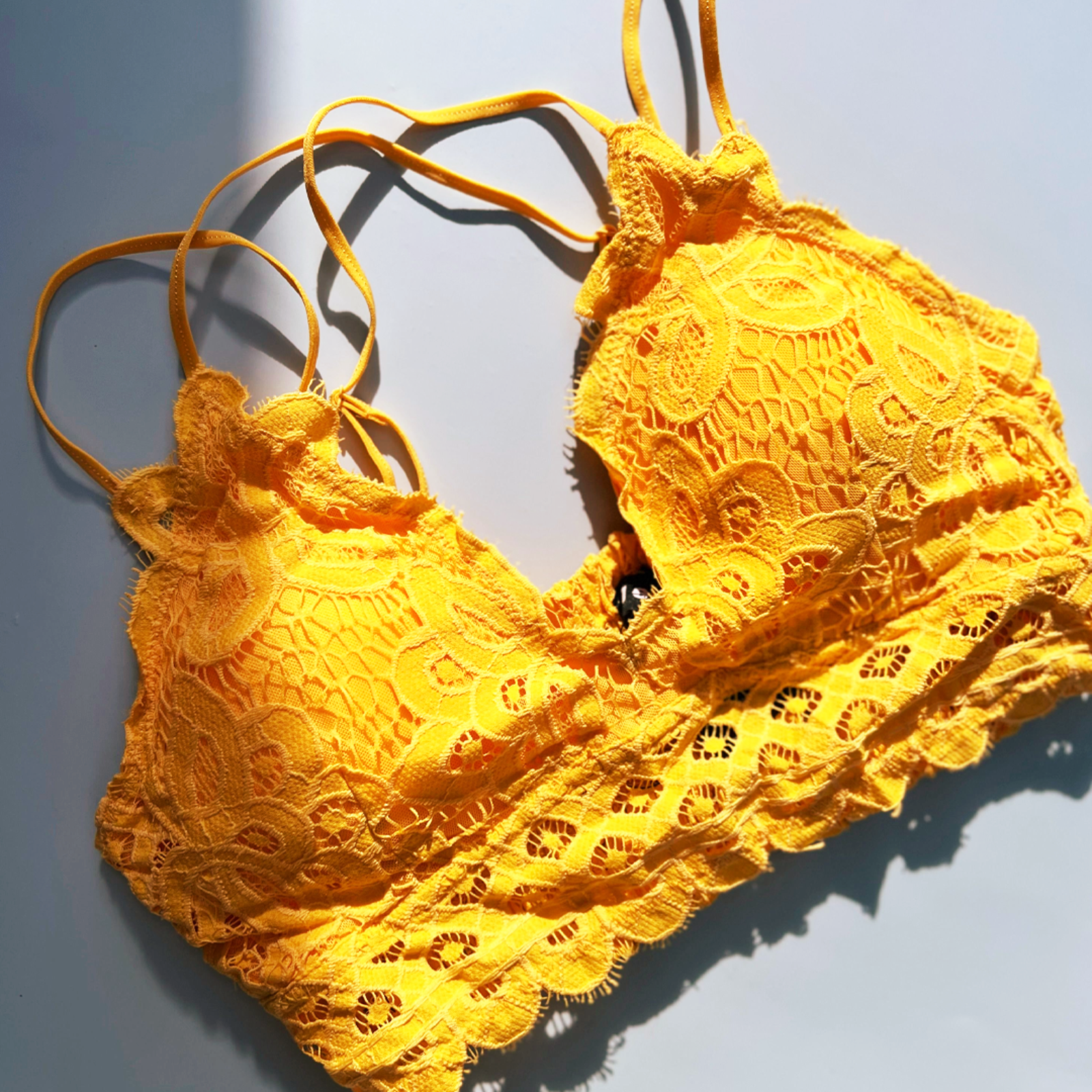 The mustard Criss-Cross Back Lace Bralette on a blue background.