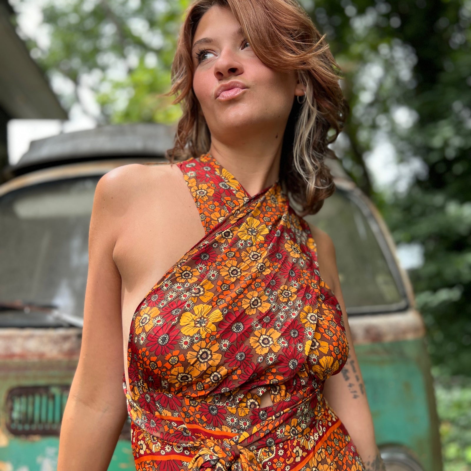 Woman wearing a patterned dress standing in front of a vintage van with greenery in the background
