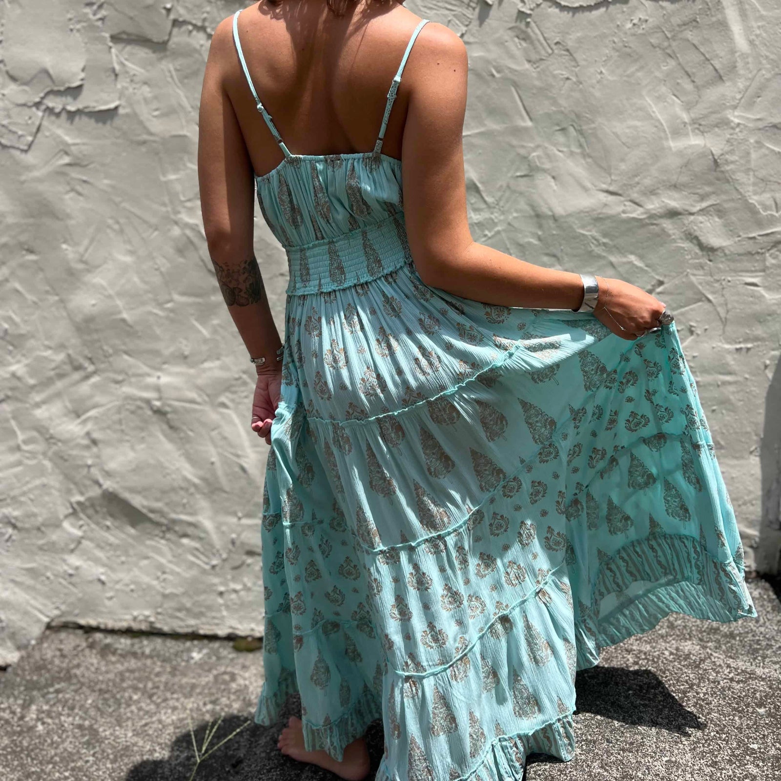 Woman wearing a light blue floral maxi dress against a textured stone wall.