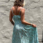 Woman wearing a light blue floral maxi boho dress against a textured wall.
