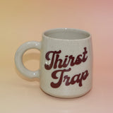 Front view of handmade mug with “Thirst Trap” in retro burgundy script