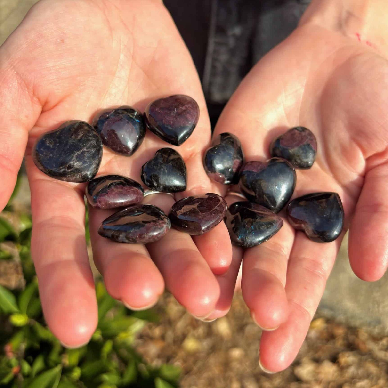 Two hands holding dark stones against a natural background