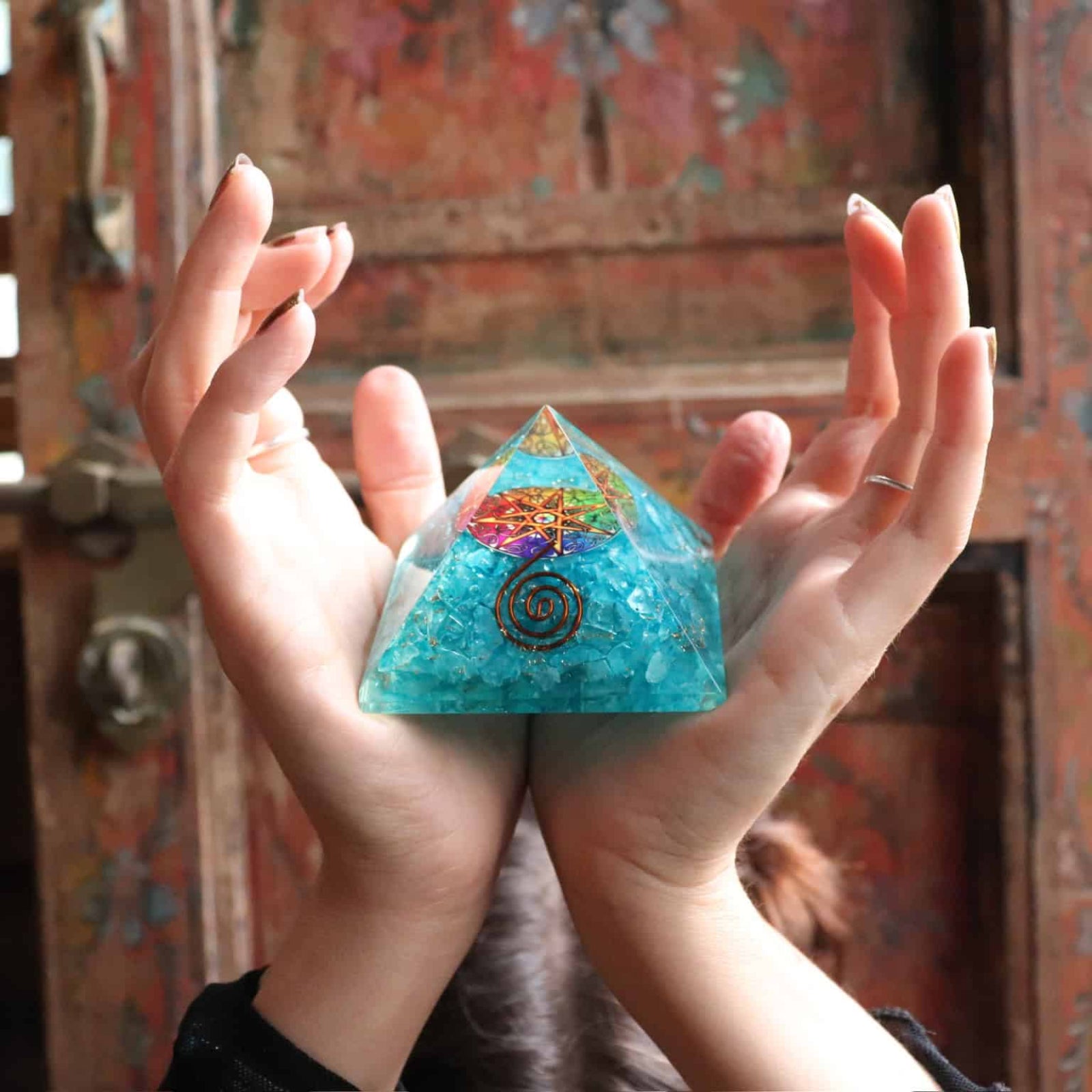 Turquoise crystal pyramid held in hands with a colorful background