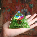 Green pyramid crystal with colorful design held in a hand against a patterned background