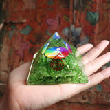 Green pyramid crystal with colorful design held in a hand against a patterned background