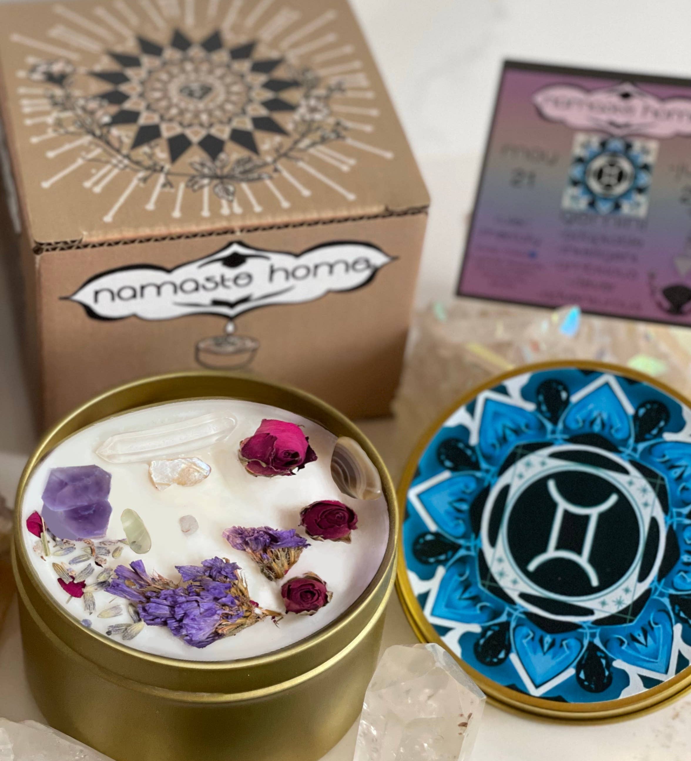 The Gemini Crystal Candle opened with the lid to the right of it. The packaging of the Gemini Crystal Candle is behind the candle next to a card
