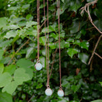 Amazonite copper crystal necklaces hanging from a tree branch against forest foliage