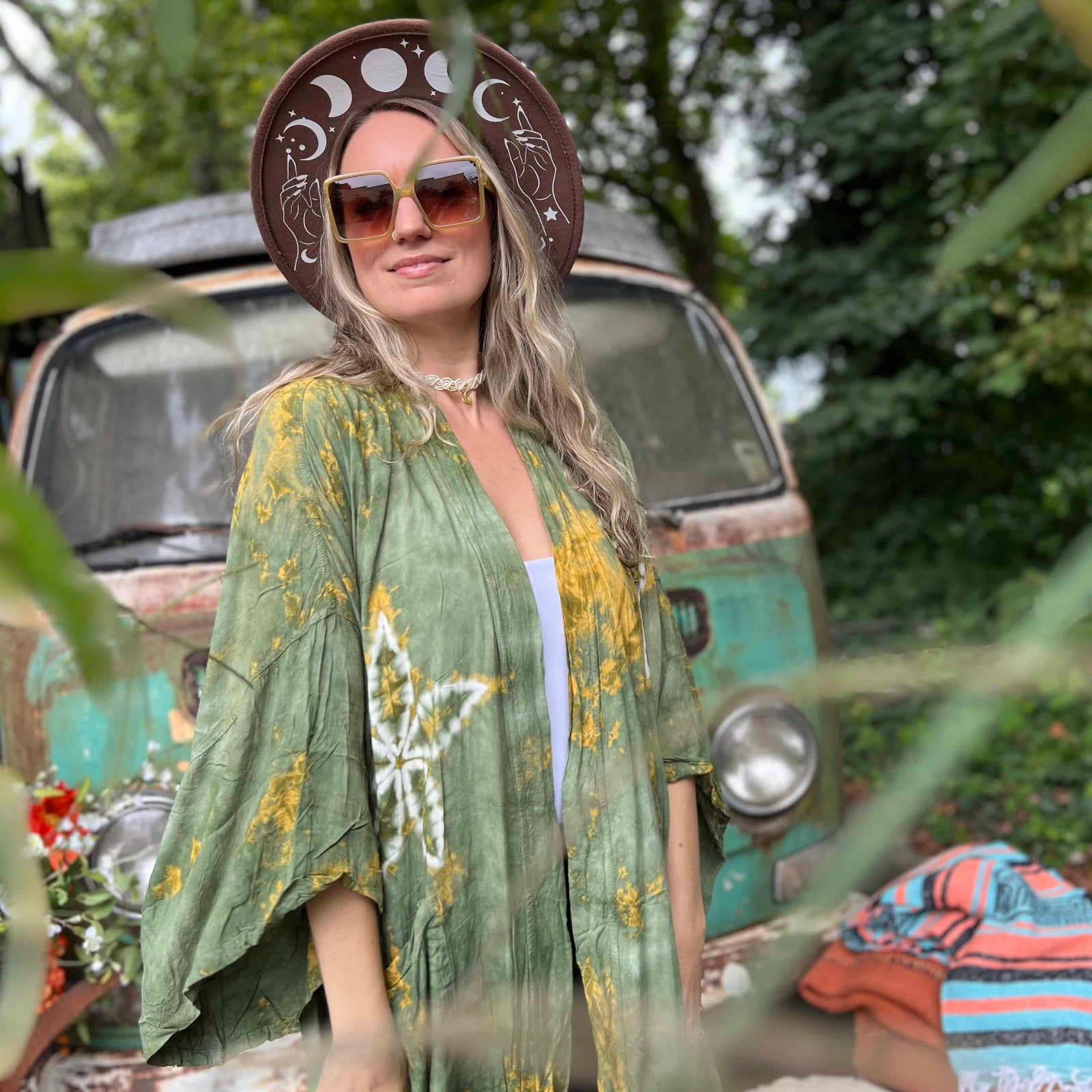 Woman in a green patterned kimono standing in front of a vintage van with a colorful blanket on it.