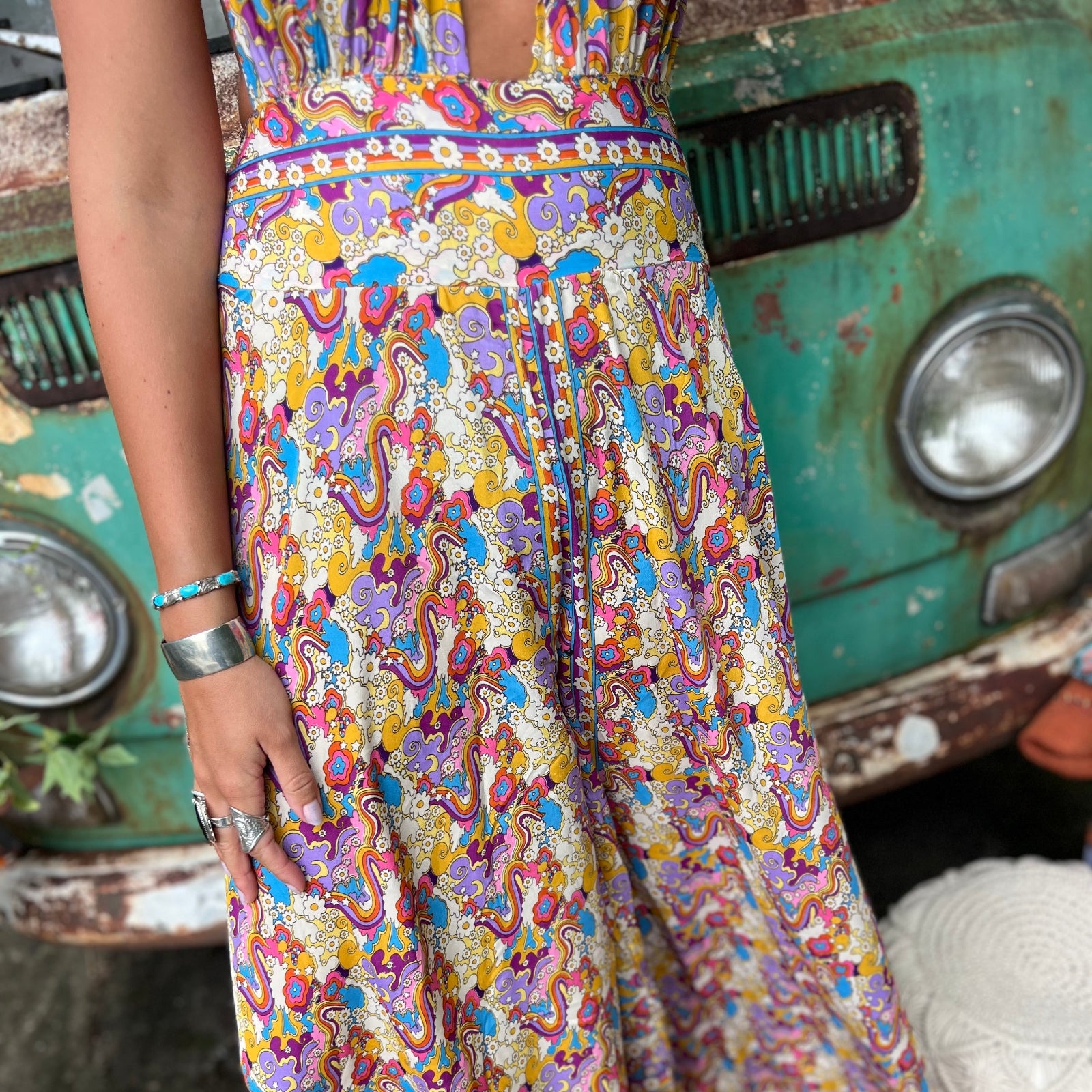 Person wearing a colorful patterned jumpsuit standing next to a vintage green truck.