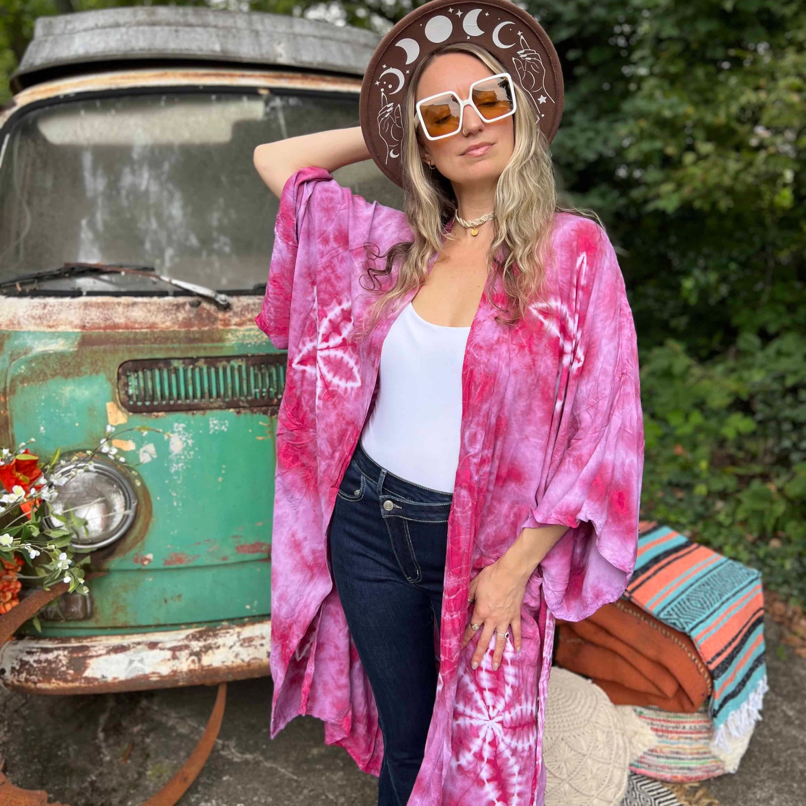 Woman in a pink tie-dye kimono standing in front of a vintage truck with a colorful rug on the ground.