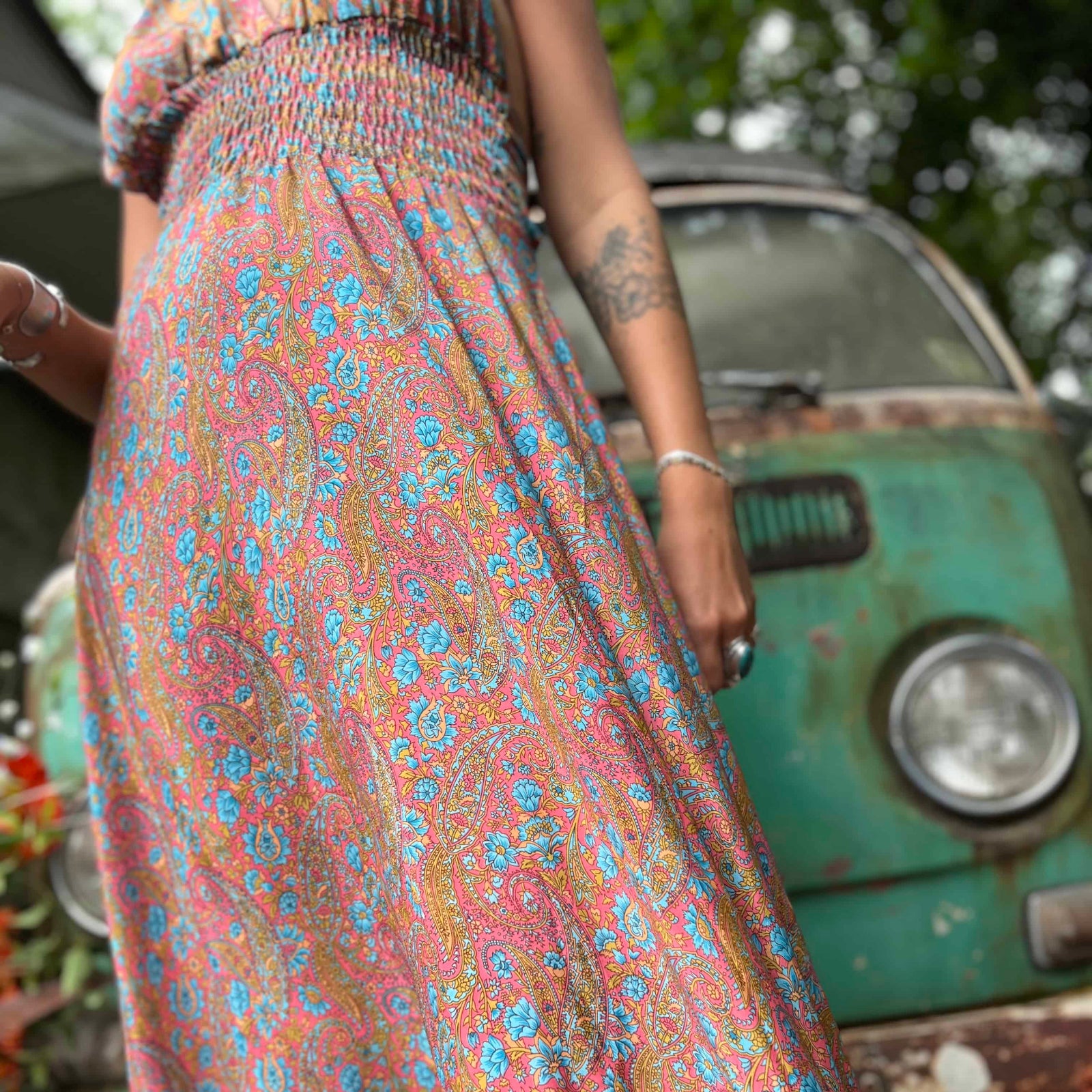 Person wearing a floral dress standing next to a vintage green car.
