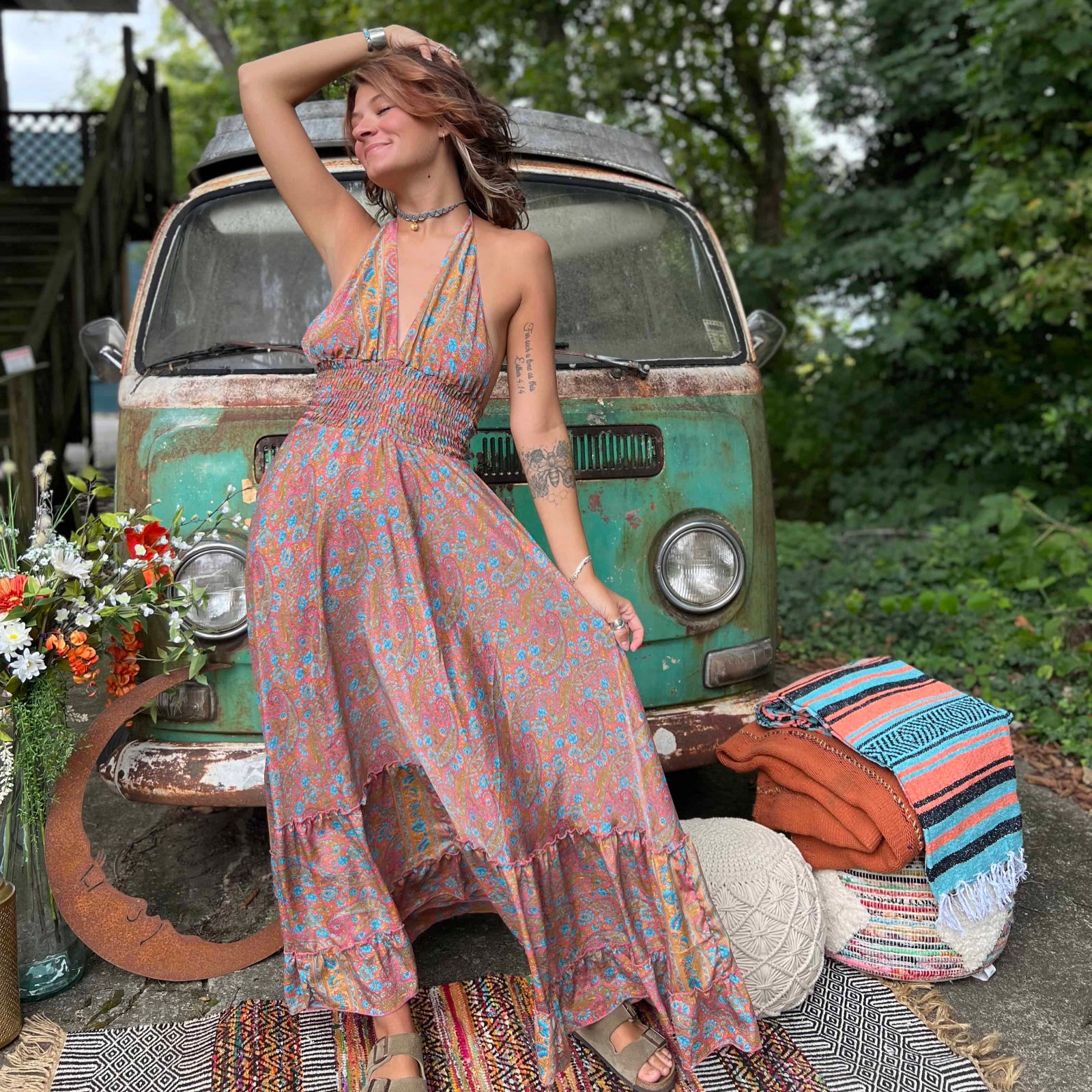 Woman in a floral dress standing in front of a vintage van with a relaxed outdoor setting.