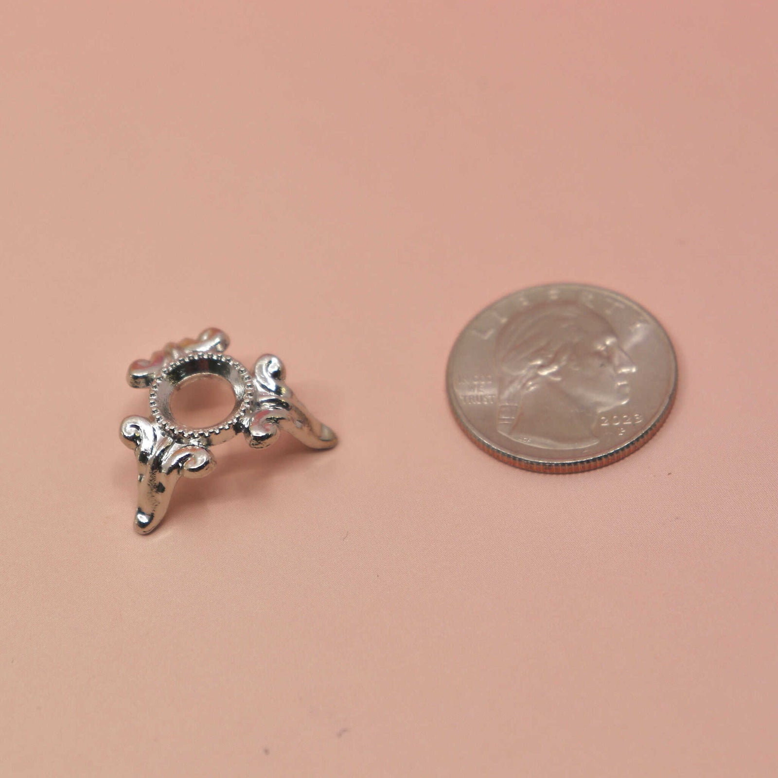 Silver sphere stand with decorative design next to a penny on a beige background