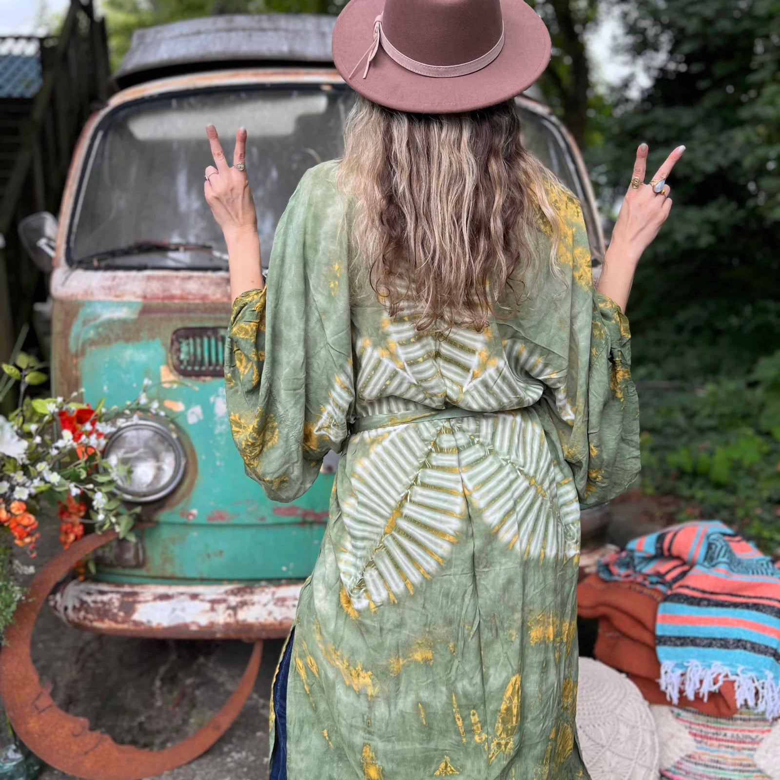 Person wearing a green patterned kimono and brown hat in front of a vintage van.