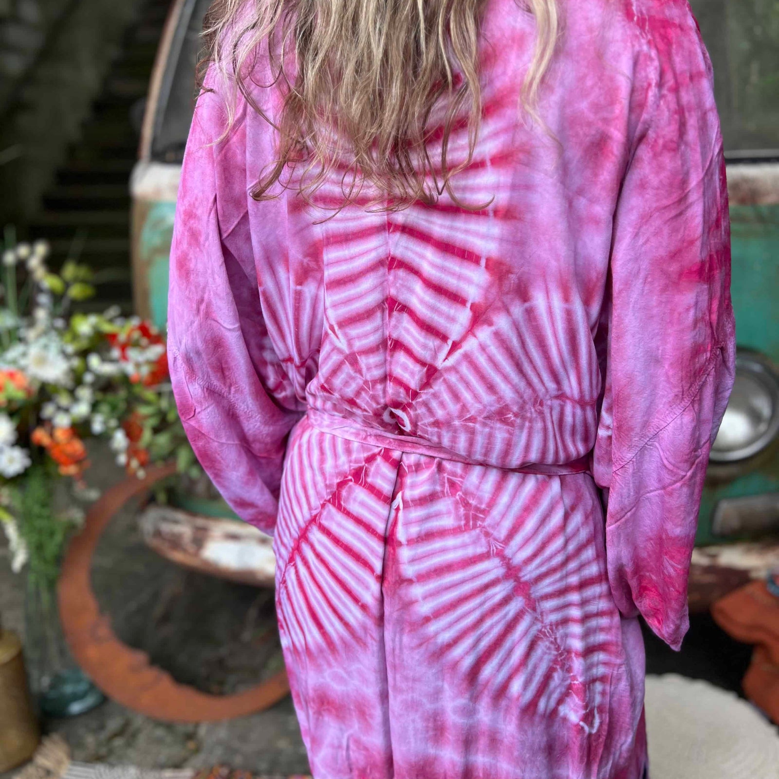 Person wearing a pink tie-dye kimono in front of a vintage vehicle.