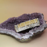 The White Sage with Palo Santo Smudge Stick 4 in. on an amethyst piece on a pink and yellow background.