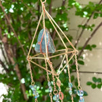 Someone holding the Amazonite Lotus Crystal Suncatcher in front of a cream-colored brick wall with greenery.