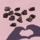 Mineral crystals arranged on a pink background with a shadow of two hands forming a heart shape.