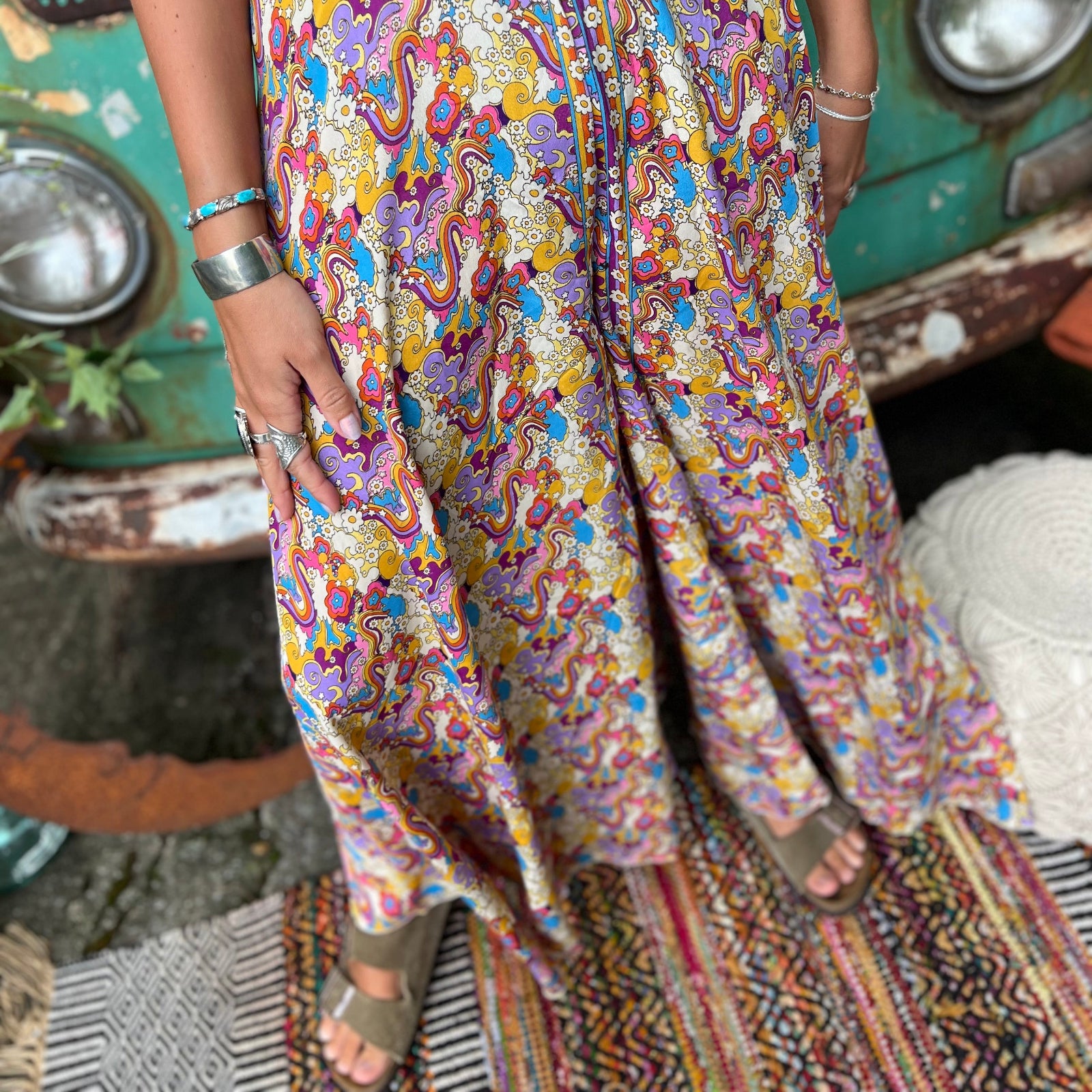 Person wearing a colorful patterned jumpsuit standing in front of a vintage vehicle.