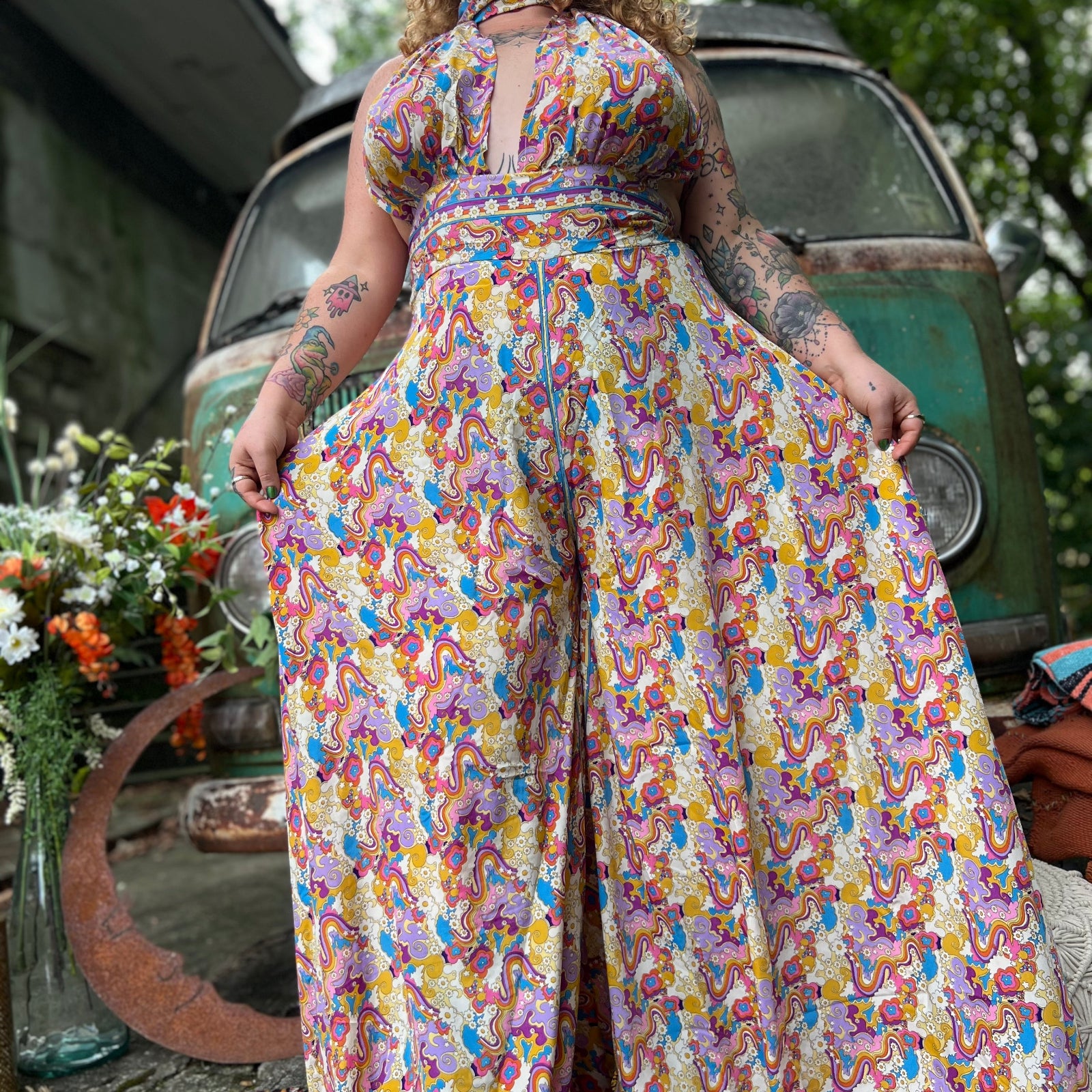 Person wearing a colorful floral jumpsuit standing in front of a vintage van.