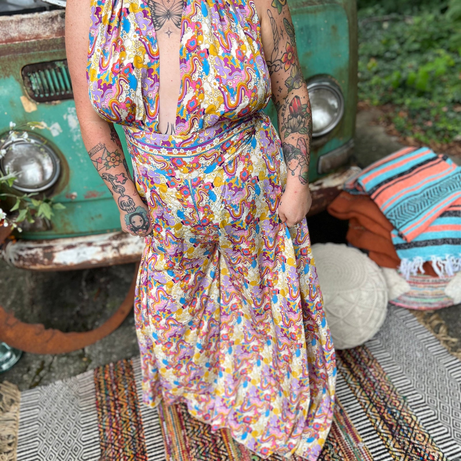 Person wearing a colorful patterned jumpsuit in front of a vintage vehicle with a relaxed outdoor setting.