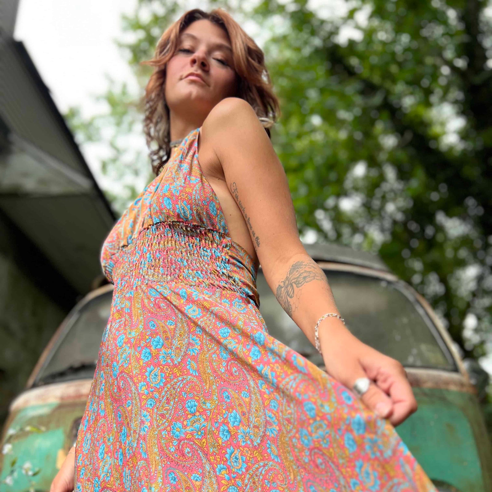 Woman in a colorful dress standing next to a vintage vehicle with trees in the background