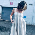 relaxed and airy babydoll midi dress in neutral blue stripes in front of brick white wall