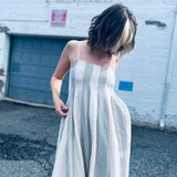 relaxed and airy babydoll midi dress in neutral blue stripes in front of brick white wall