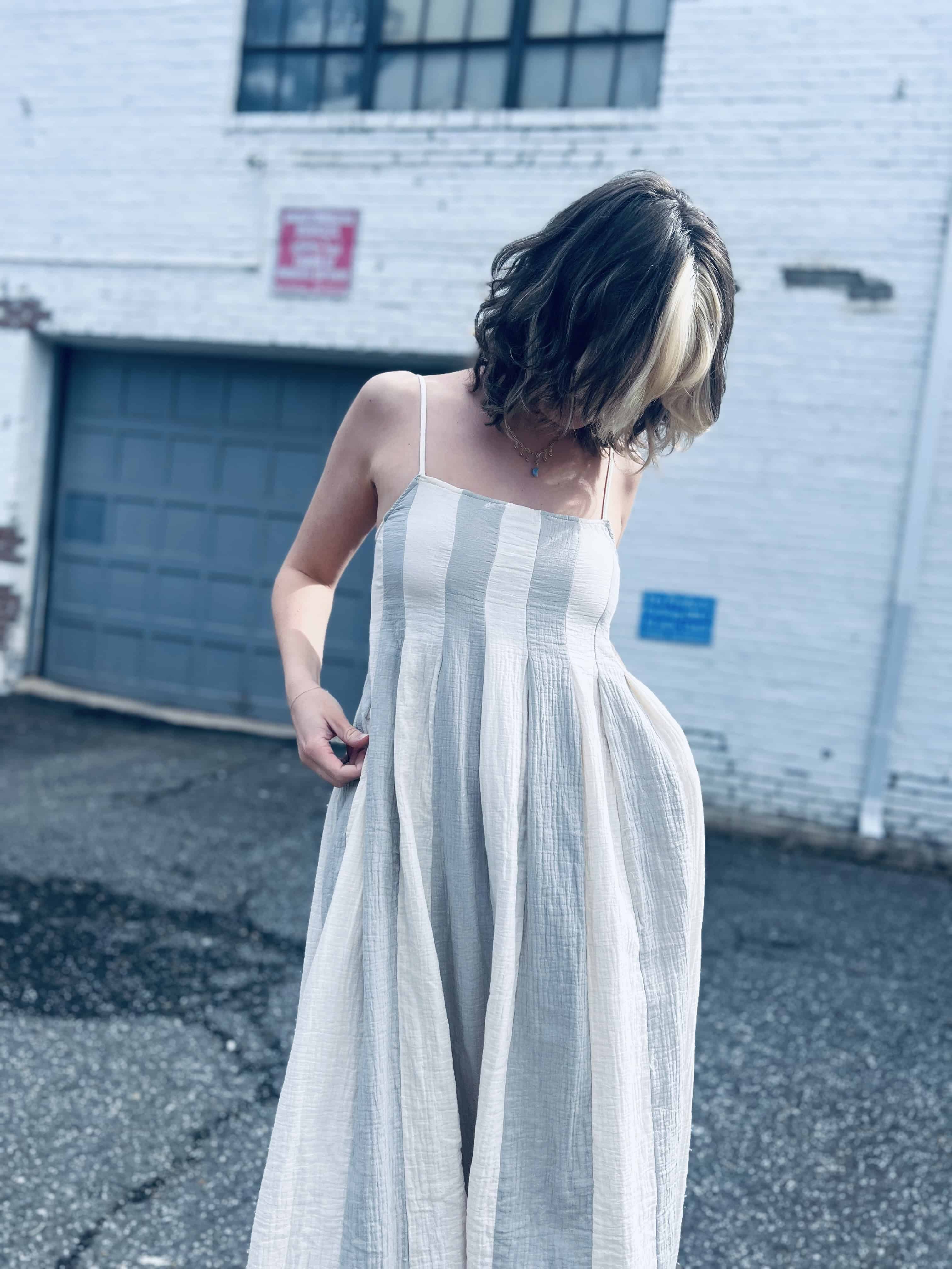 relaxed and airy babydoll midi dress in neutral blue stripes in front of brick white wall