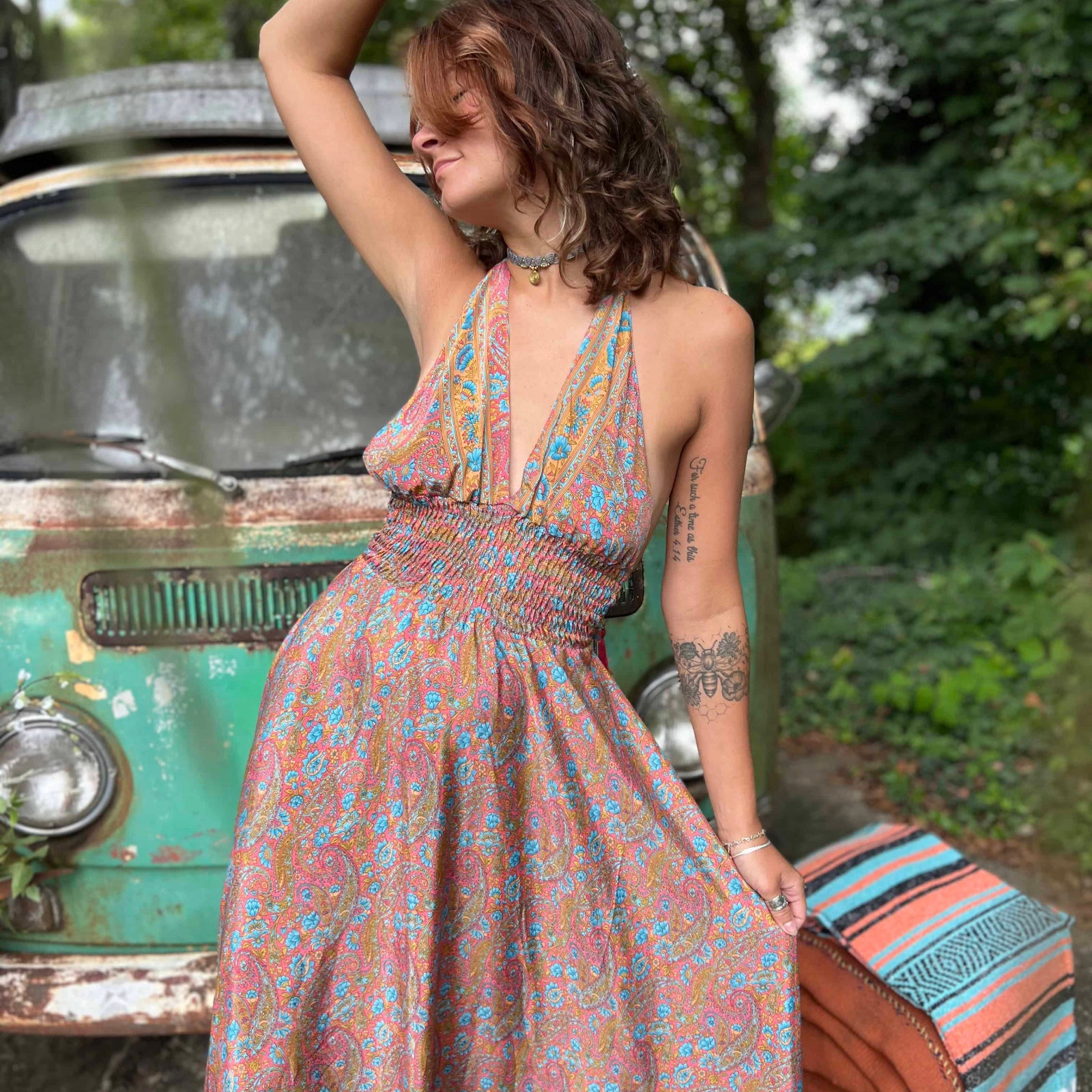Woman in a floral dress standing next to a vintage van in a natural setting