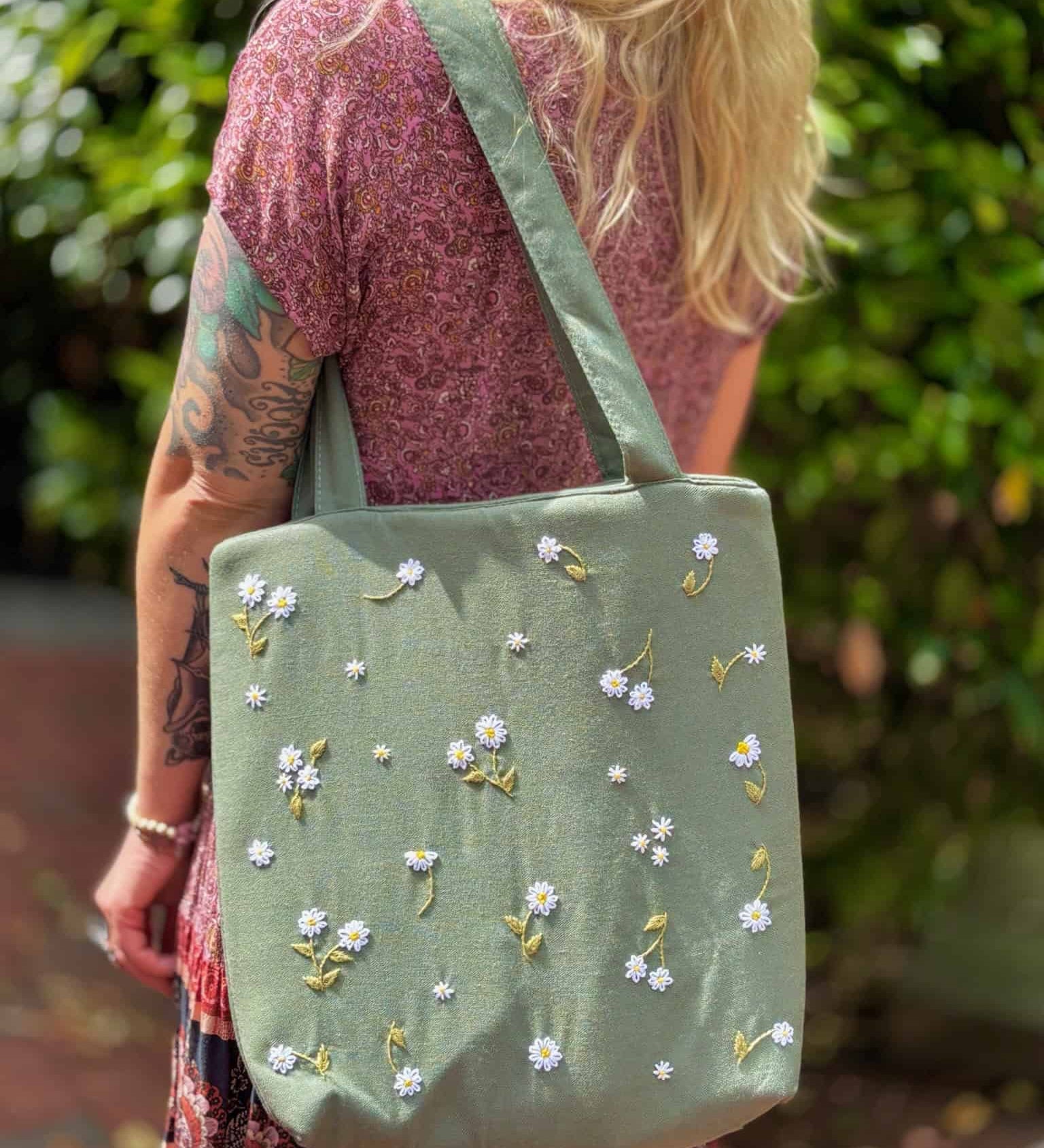 Blonde woman wearing a floral dress and carrying a sage green linen tote bag with hand-embroidered white daisies
