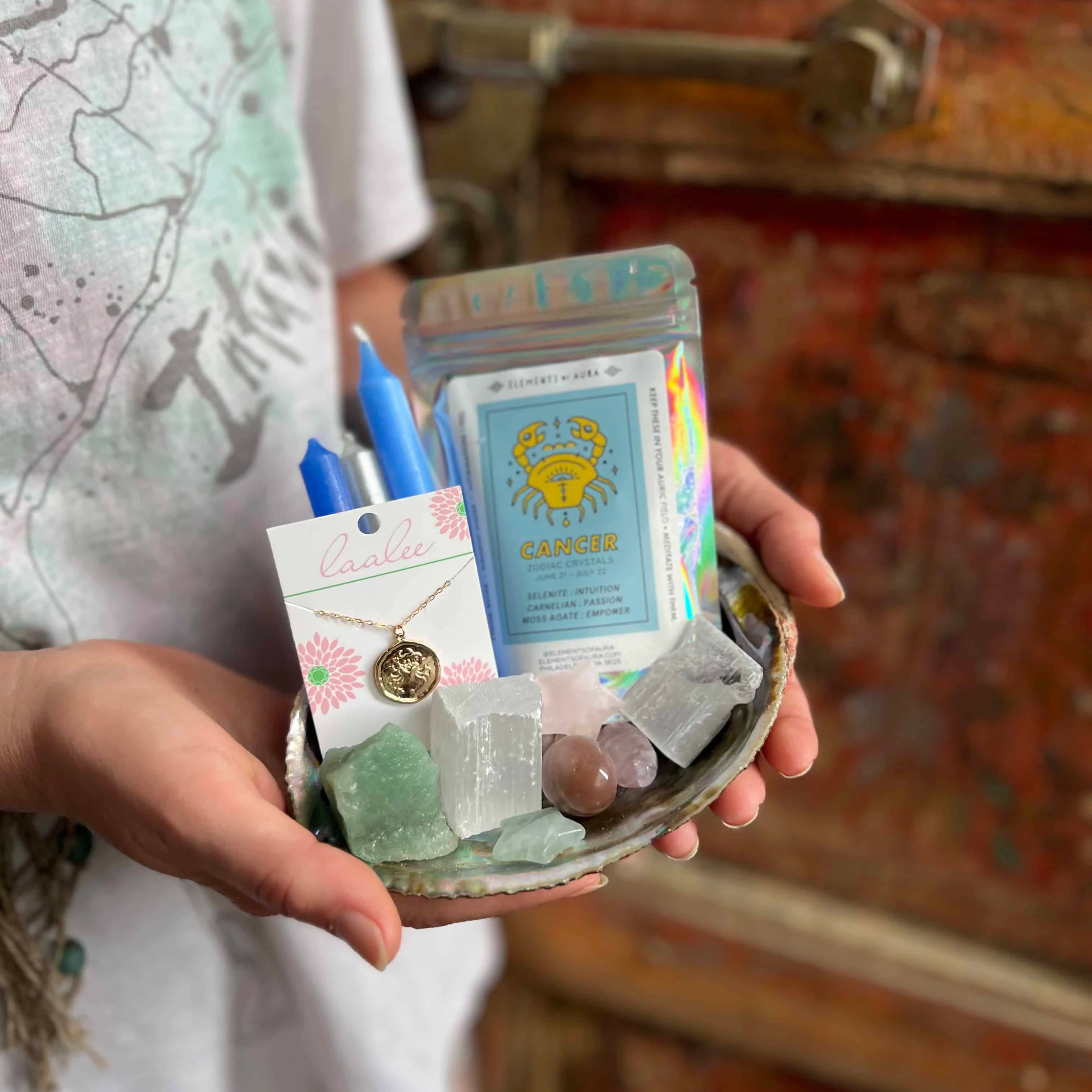person holding a plate of cancer zodiac gifts such as a cancer charm necklace, crystals for cancers, and blue chime candles