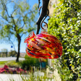 Colorful handblown art glass hummingbird feeder hanging outdoors in garden
