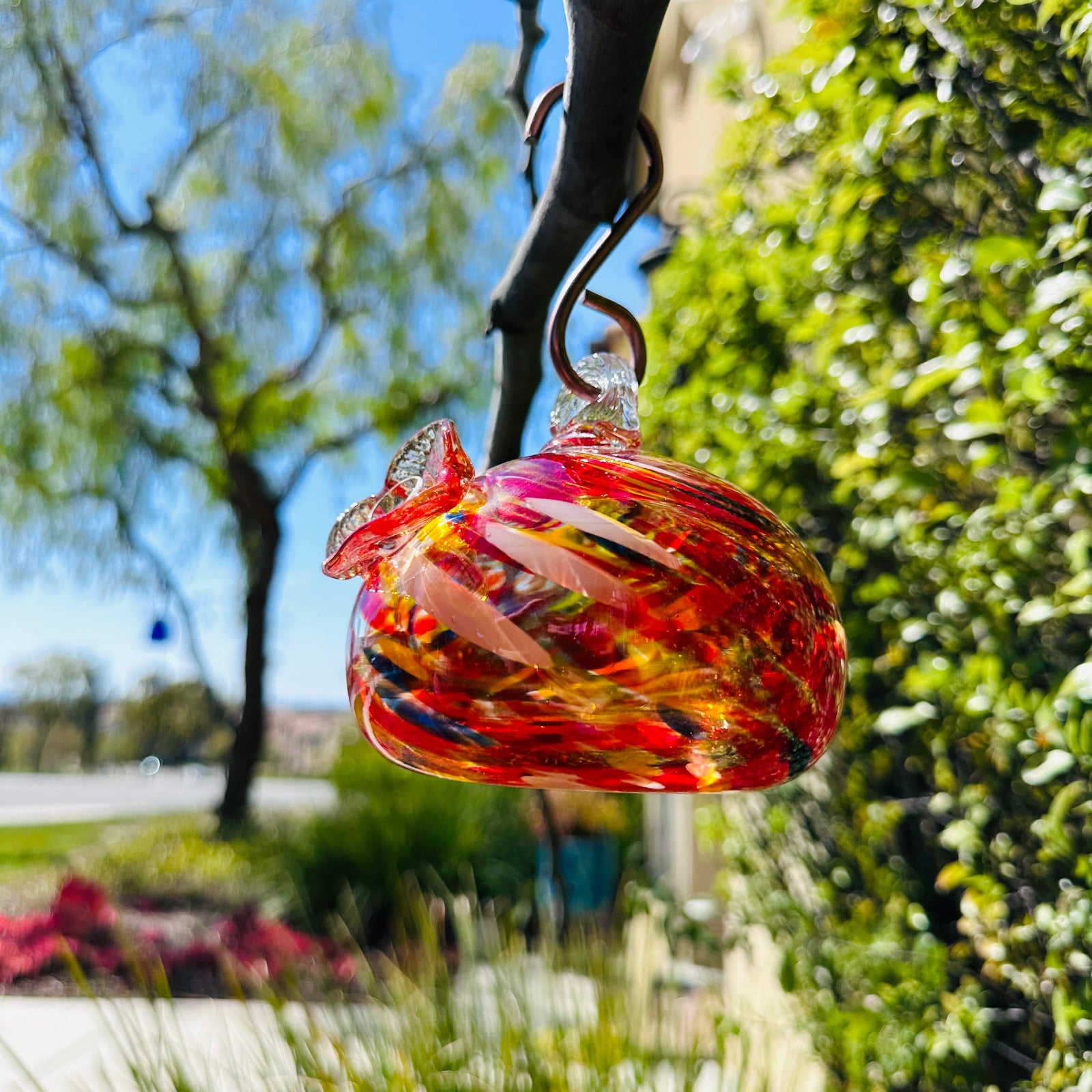 Colorful handblown art glass hummingbird feeder hanging outdoors in garden