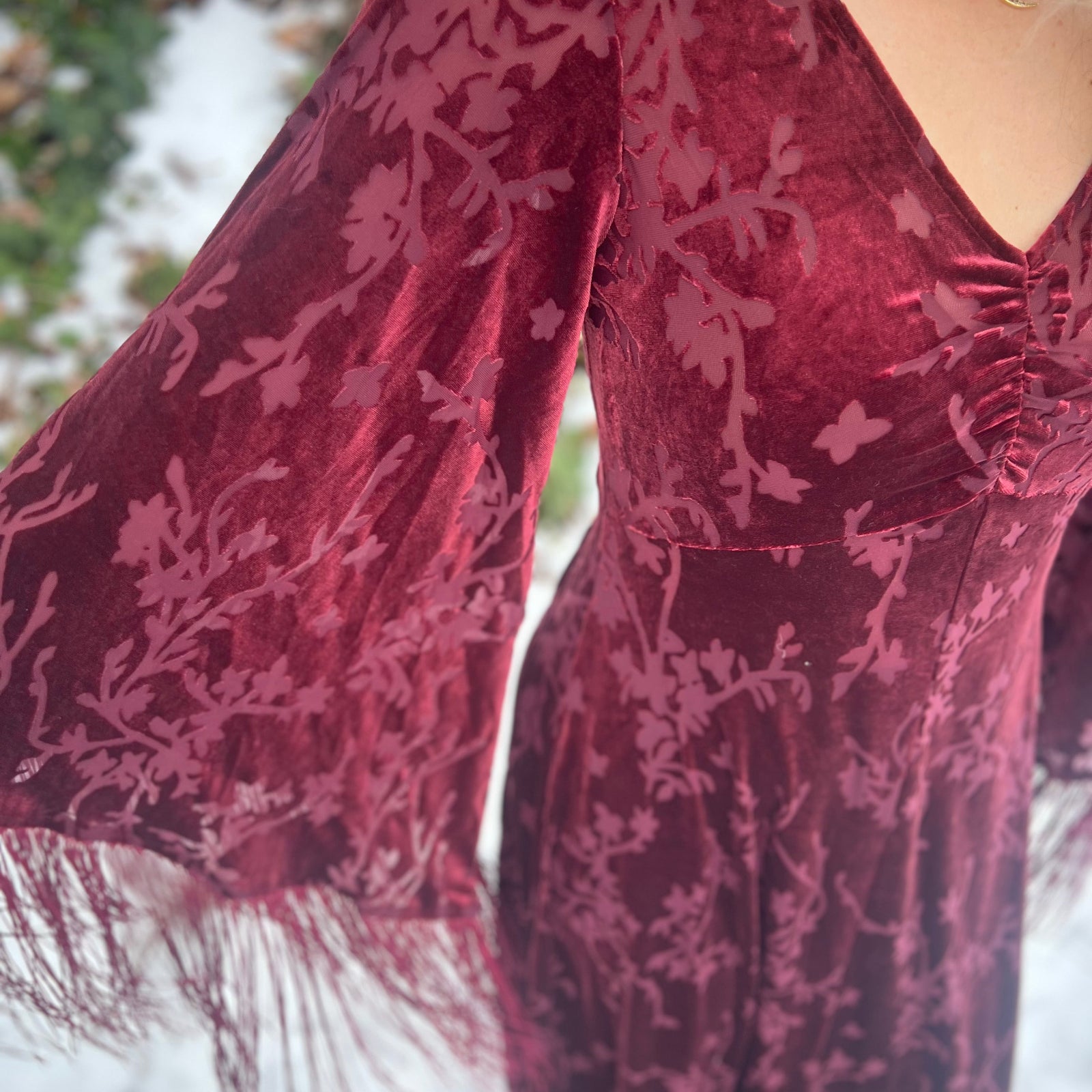 Close-up of a burgundy velvet dress with floral patterns in a snowy outdoor setting.