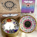The Aquarius Crystal Candle opened with the lid to the right of it. The packaging of the Aquarius Crystal Candle is behind the candle next to an Aquarius info card.